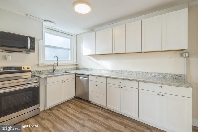 kitchen featuring light stone countertops, stainless steel appliances, light wood finished floors, a sink, and white cabinetry