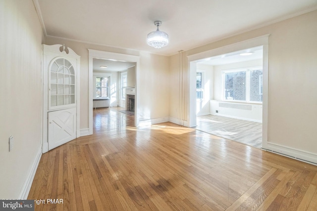 unfurnished dining area with radiator, ornamental molding, light hardwood / wood-style flooring, and a brick fireplace