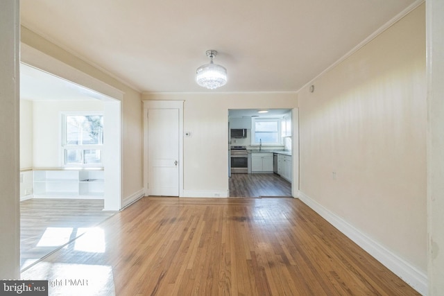 unfurnished room with crown molding, a sink, light wood-style flooring, and baseboards