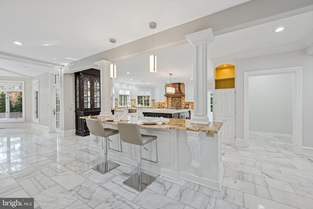 kitchen with extractor fan, kitchen peninsula, light stone countertops, decorative light fixtures, and ornate columns