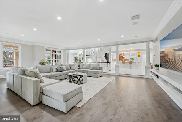 living room featuring decorative columns, an inviting chandelier, light hardwood / wood-style floors, and crown molding