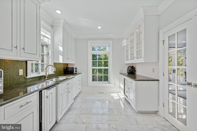 kitchen featuring dark stone counters, decorative backsplash, sink, crown molding, and white cabinetry