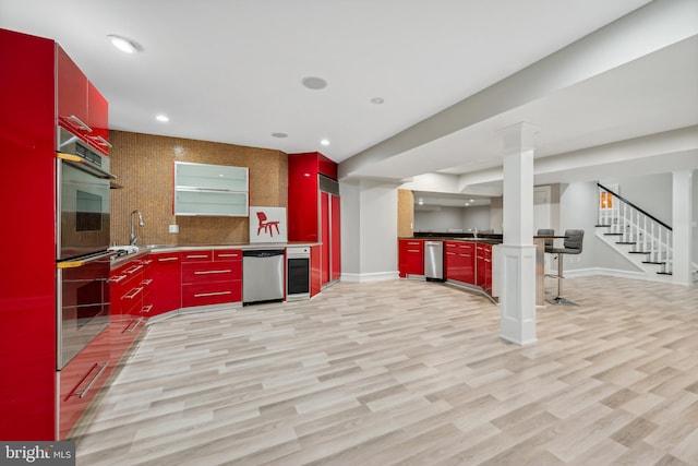 kitchen with stainless steel appliances, light hardwood / wood-style floors, sink, and decorative columns