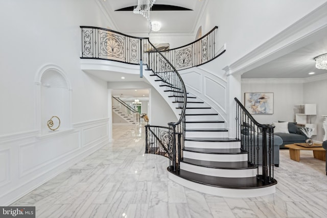 stairway with a towering ceiling, an inviting chandelier, and crown molding