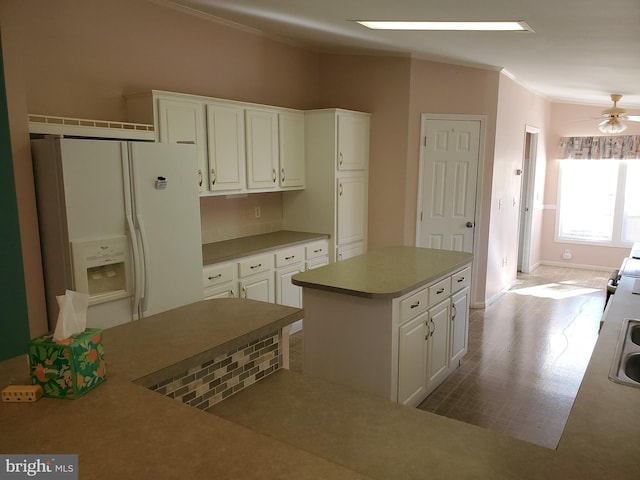 kitchen featuring ceiling fan, white fridge with ice dispenser, a kitchen island, white cabinetry, and ornamental molding