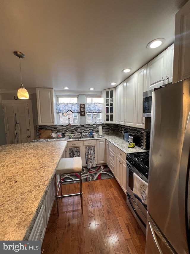 kitchen featuring pendant lighting, dark wood-type flooring, decorative backsplash, white cabinetry, and stainless steel appliances