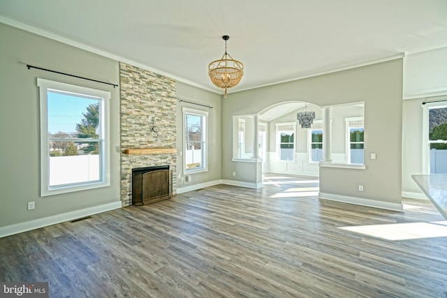 unfurnished living room featuring hardwood / wood-style flooring, a stone fireplace, ornate columns, and crown molding