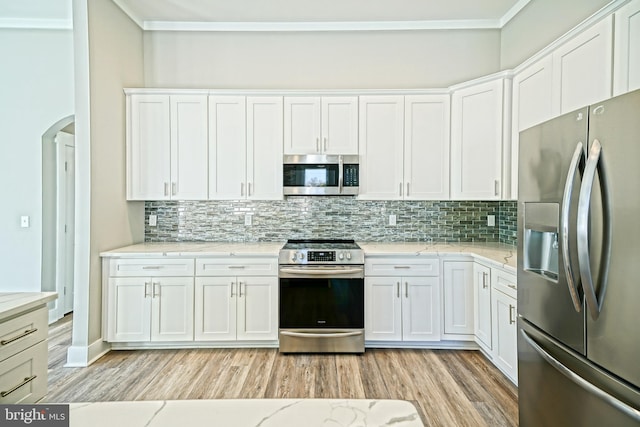 kitchen with appliances with stainless steel finishes, light wood-type flooring, tasteful backsplash, and white cabinetry