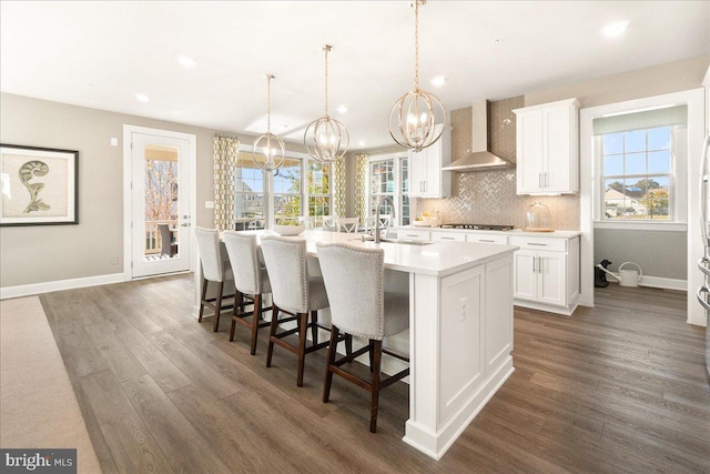 kitchen featuring white cabinetry, wall chimney range hood, a kitchen island with sink, and a wealth of natural light