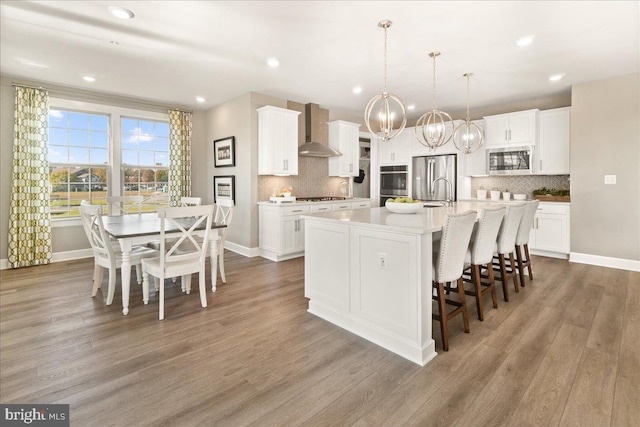 kitchen with white cabinetry, a kitchen island with sink, wall chimney exhaust hood, and stainless steel appliances