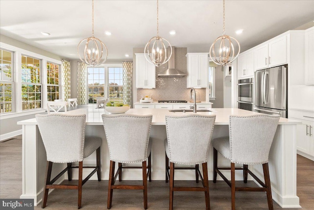 kitchen with hanging light fixtures, stainless steel appliances, wall chimney range hood, a breakfast bar, and a center island with sink