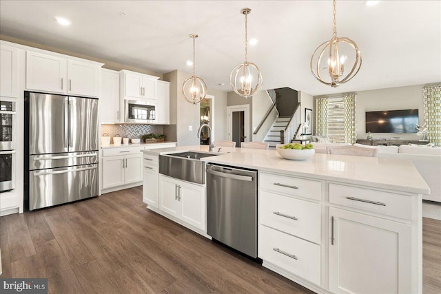 kitchen with stainless steel appliances, sink, white cabinets, dark hardwood / wood-style floors, and an island with sink