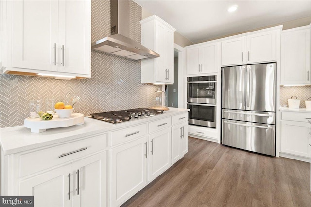 kitchen with wall chimney range hood, dark hardwood / wood-style floors, tasteful backsplash, white cabinetry, and stainless steel appliances