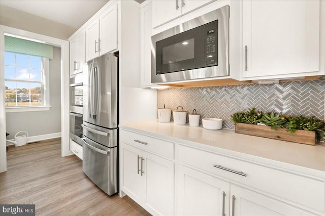 kitchen featuring tasteful backsplash, white cabinetry, stainless steel appliances, and light hardwood / wood-style floors