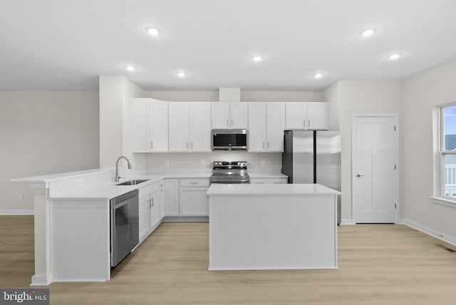 kitchen featuring kitchen peninsula, stainless steel appliances, a kitchen island, white cabinetry, and sink