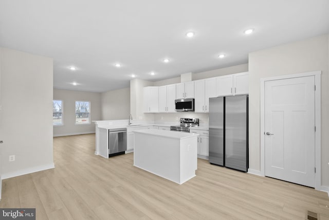 kitchen with kitchen peninsula, stainless steel appliances, light wood-type flooring, white cabinets, and sink