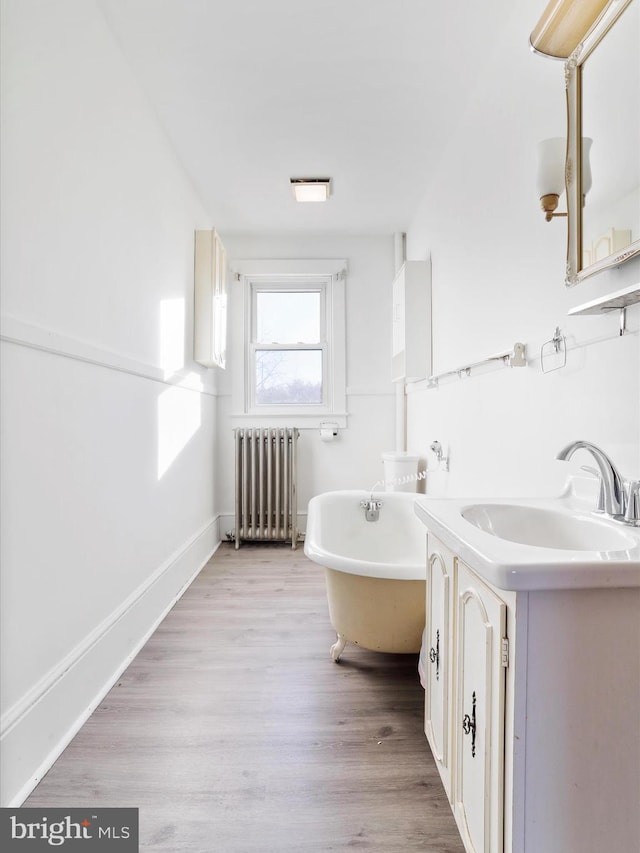 bathroom featuring hardwood / wood-style flooring, vanity, a bath, and radiator