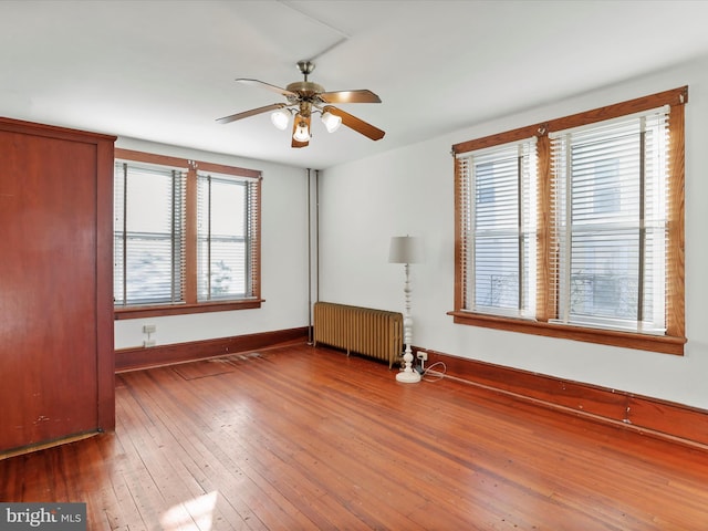 interior space featuring radiator heating unit, ceiling fan, multiple windows, and wood-type flooring