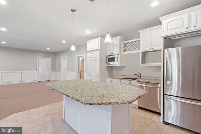 kitchen with hanging light fixtures, light carpet, stainless steel appliances, white cabinets, and light stone counters