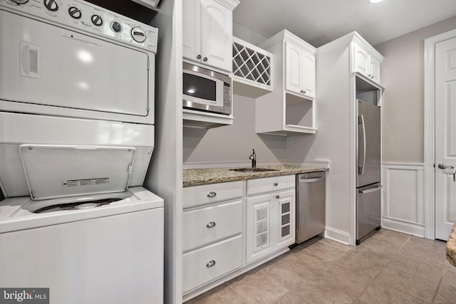 kitchen with stacked washer / drying machine, sink, light stone countertops, white cabinetry, and appliances with stainless steel finishes