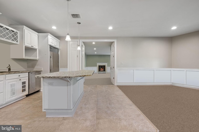 kitchen featuring appliances with stainless steel finishes, a kitchen island, white cabinetry, light carpet, and decorative light fixtures