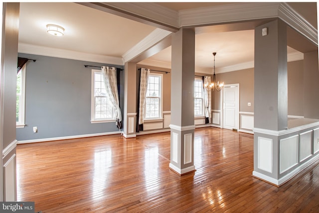 empty room with a chandelier, hardwood / wood-style floors, decorative columns, and ornamental molding