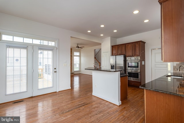 kitchen with appliances with stainless steel finishes, tasteful backsplash, dark stone counters, and wood-type flooring