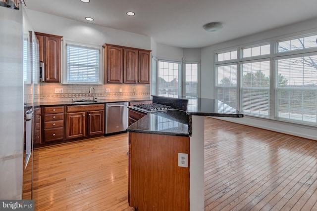 kitchen with sink, dishwasher, light hardwood / wood-style flooring, backsplash, and dark stone countertops