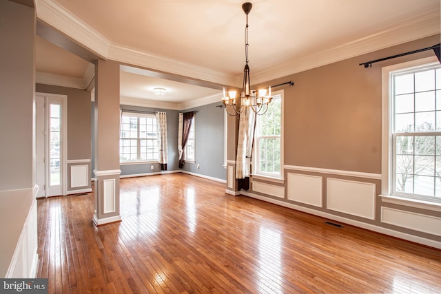 unfurnished dining area with ornate columns, crown molding, a notable chandelier, and hardwood / wood-style flooring