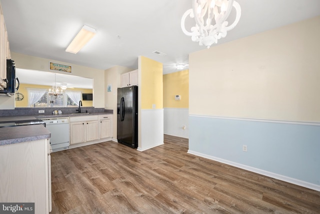 kitchen featuring hanging light fixtures, an inviting chandelier, hardwood / wood-style flooring, black appliances, and sink