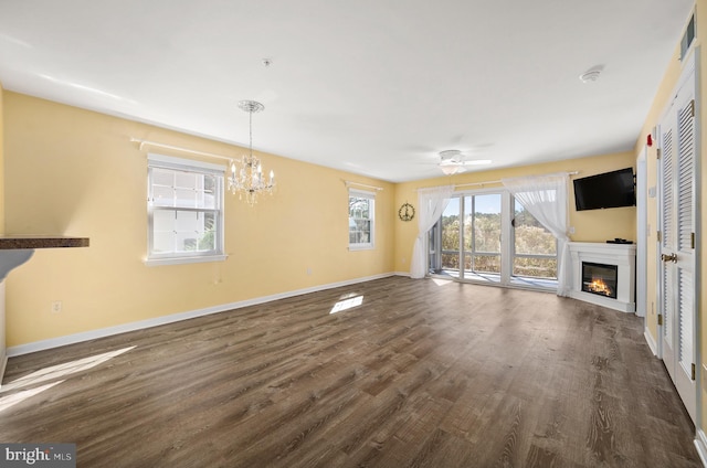 unfurnished living room featuring a healthy amount of sunlight, dark hardwood / wood-style flooring, and ceiling fan with notable chandelier