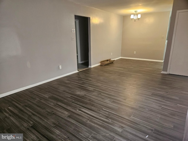 empty room with dark hardwood / wood-style flooring and an inviting chandelier