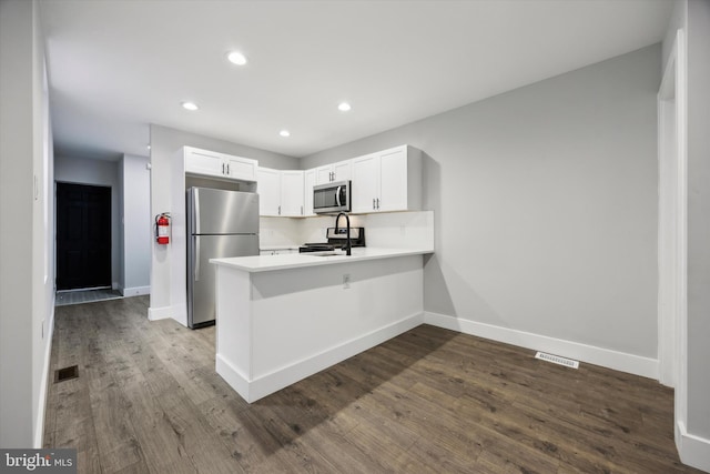 kitchen featuring hardwood / wood-style flooring, kitchen peninsula, stainless steel appliances, sink, and white cabinets