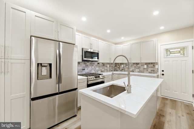 kitchen featuring an island with sink, white cabinets, appliances with stainless steel finishes, light stone counters, and light hardwood / wood-style floors