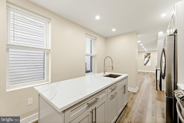 kitchen with light hardwood / wood-style flooring, sink, light stone counters, and an island with sink