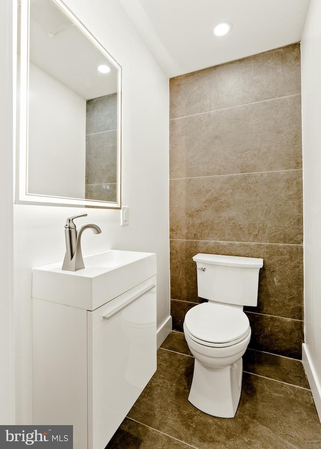 bathroom with toilet, vanity, tile walls, and tile patterned flooring