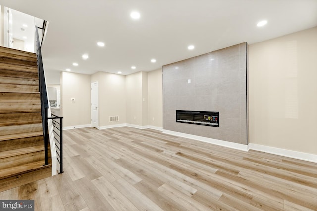 basement with a tile fireplace and light wood-type flooring