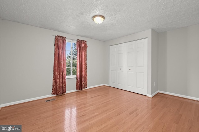 unfurnished bedroom with light wood-type flooring, a textured ceiling, and a closet