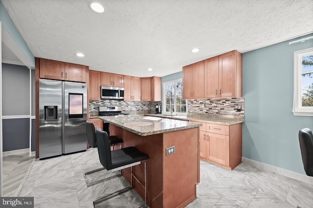 kitchen with a kitchen bar, light stone counters, a textured ceiling, stainless steel appliances, and a center island