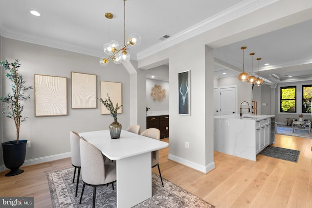 dining space with crown molding, sink, light wood-type flooring, and a chandelier