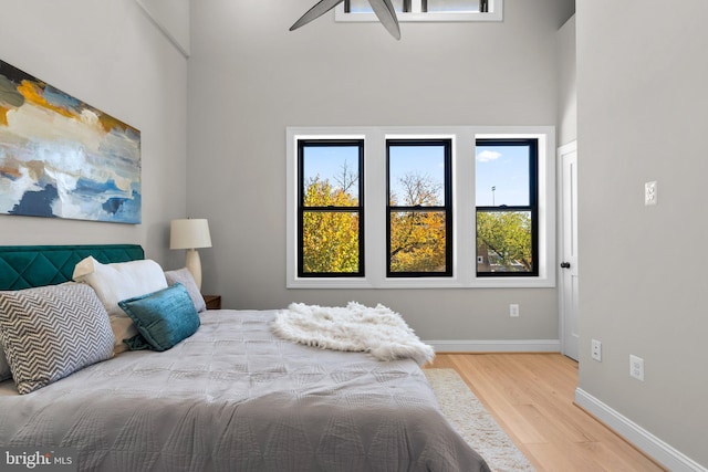 bedroom with ceiling fan, a towering ceiling, and hardwood / wood-style floors