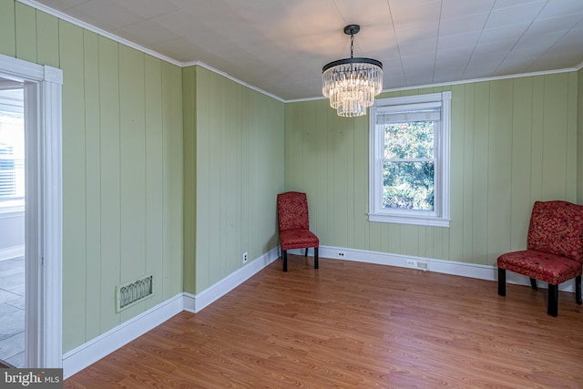 sitting room with ornamental molding, a notable chandelier, wood walls, and hardwood / wood-style flooring