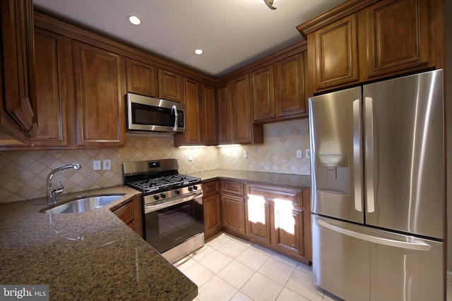 kitchen with dark stone counters, sink, tasteful backsplash, light tile patterned flooring, and stainless steel appliances