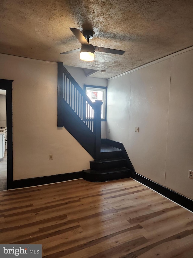 stairway featuring a textured ceiling, wood-type flooring, and ceiling fan