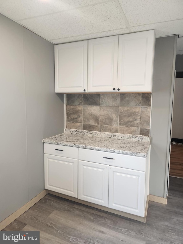 kitchen with decorative backsplash, white cabinetry, a paneled ceiling, and hardwood / wood-style flooring