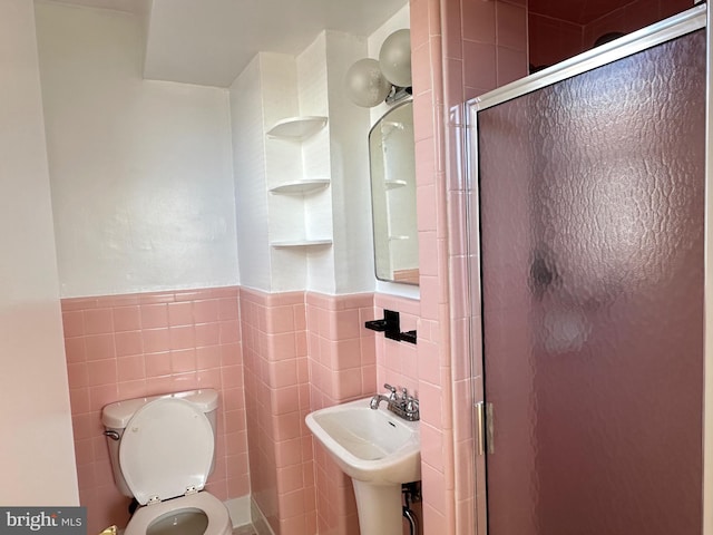 bathroom with a shower with door, tile walls, sink, and toilet