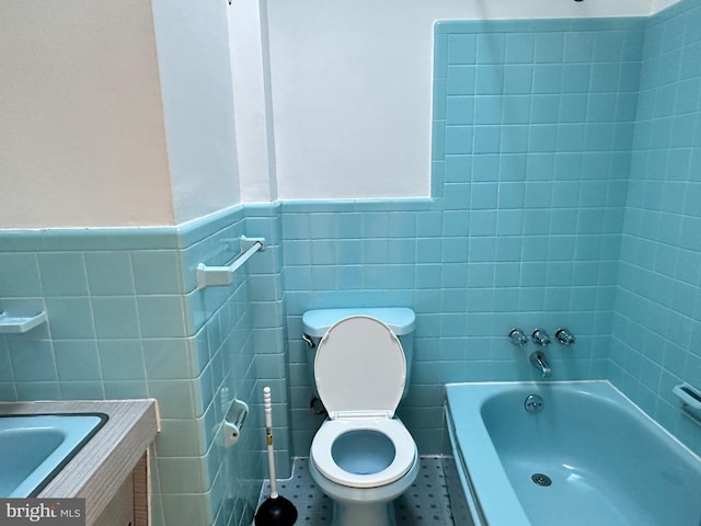 bathroom featuring tile patterned floors, toilet, a bathing tub, tile walls, and vanity