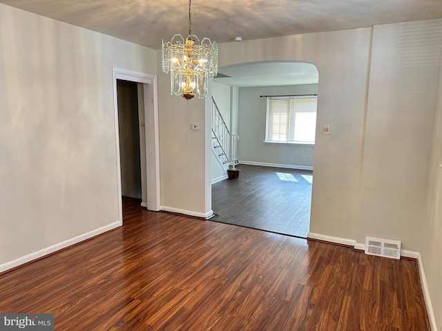 spare room with a notable chandelier and dark hardwood / wood-style floors