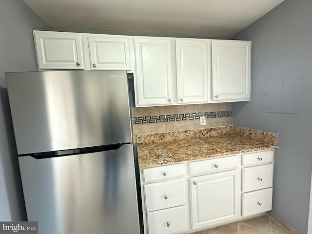 kitchen featuring white cabinets, backsplash, and stainless steel refrigerator