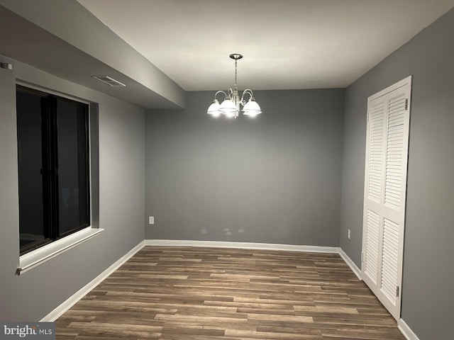 spare room featuring a notable chandelier and dark wood-type flooring